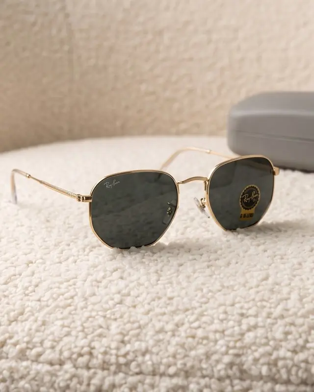 Gold Ray-Ban hexagonal sunglasses on a cream bouclé chair